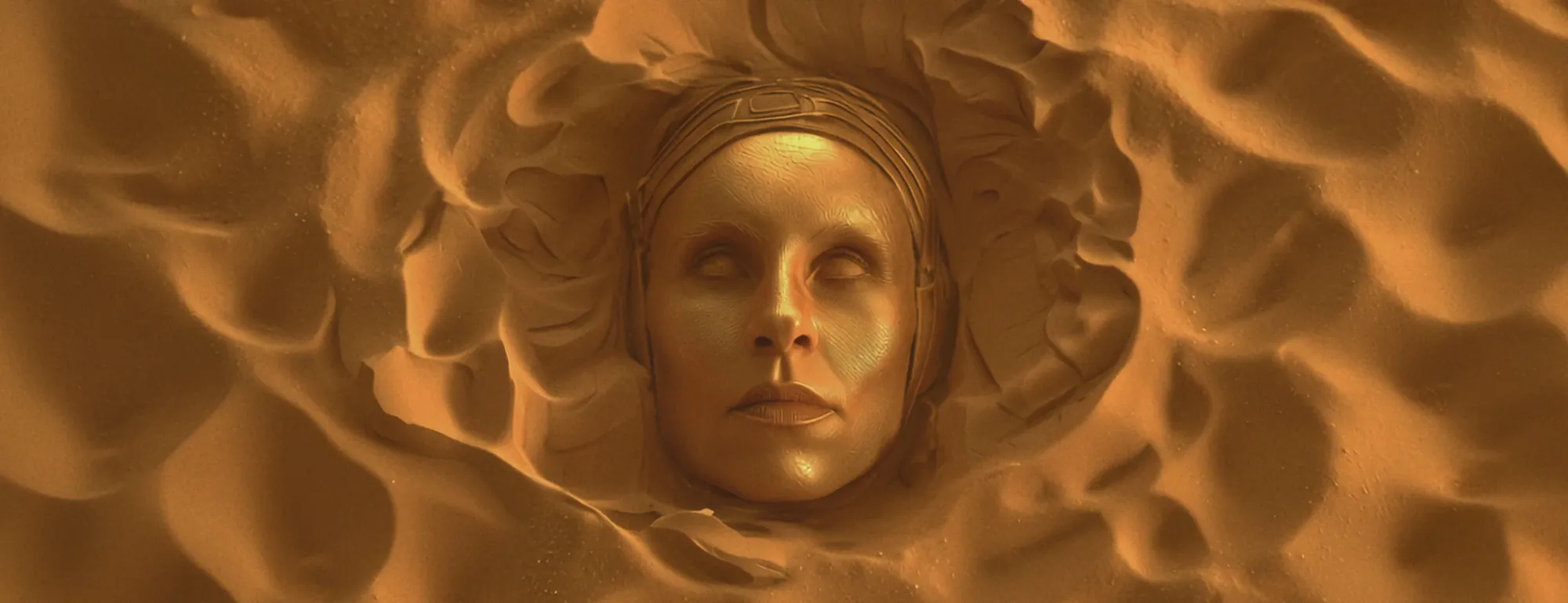 Screen content: a golden face rising out of desert sand